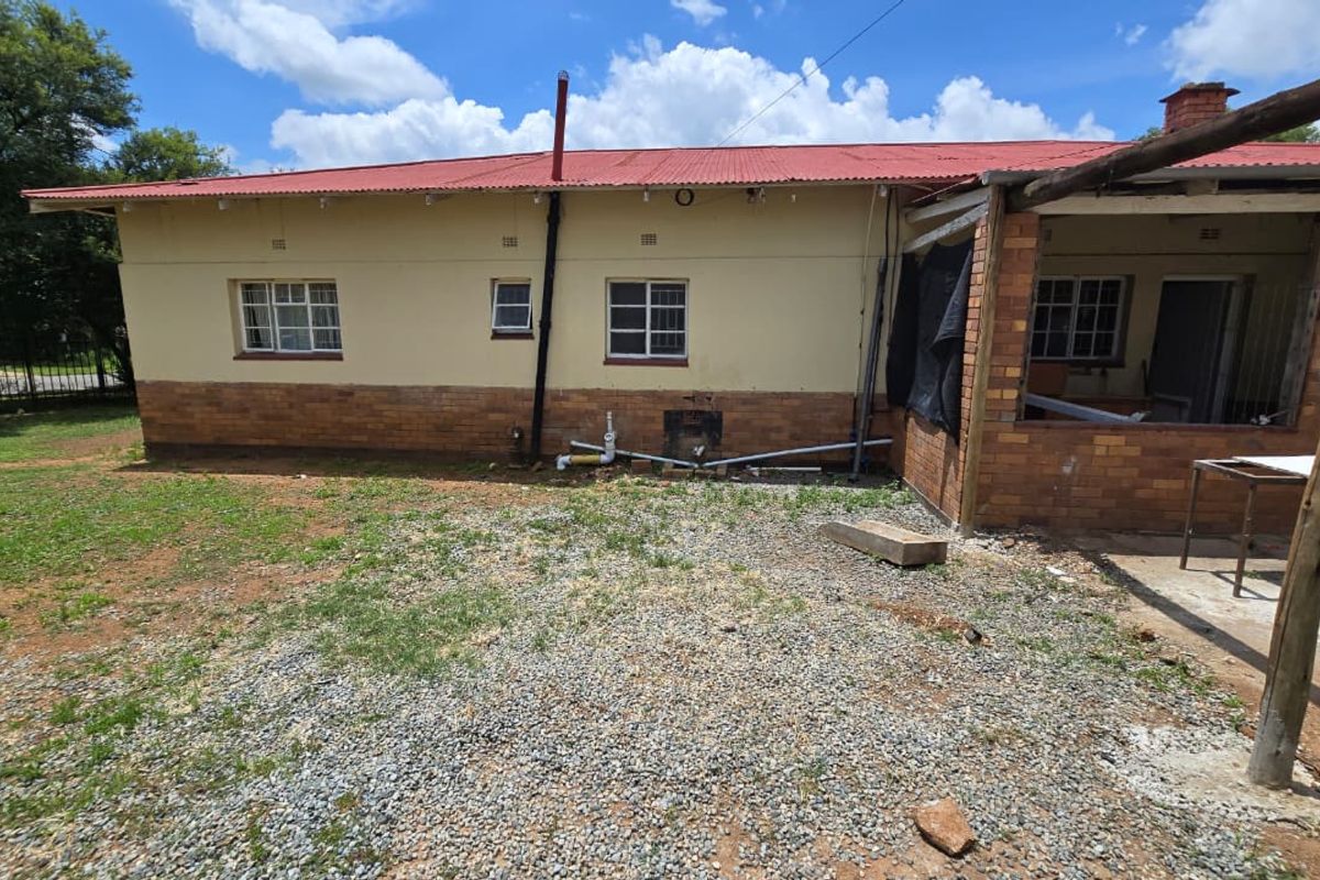 Rear view of the property featuring a corrugated metal roof, brick facade, and a partially covered patio area with exposed plumbing infrastructure.