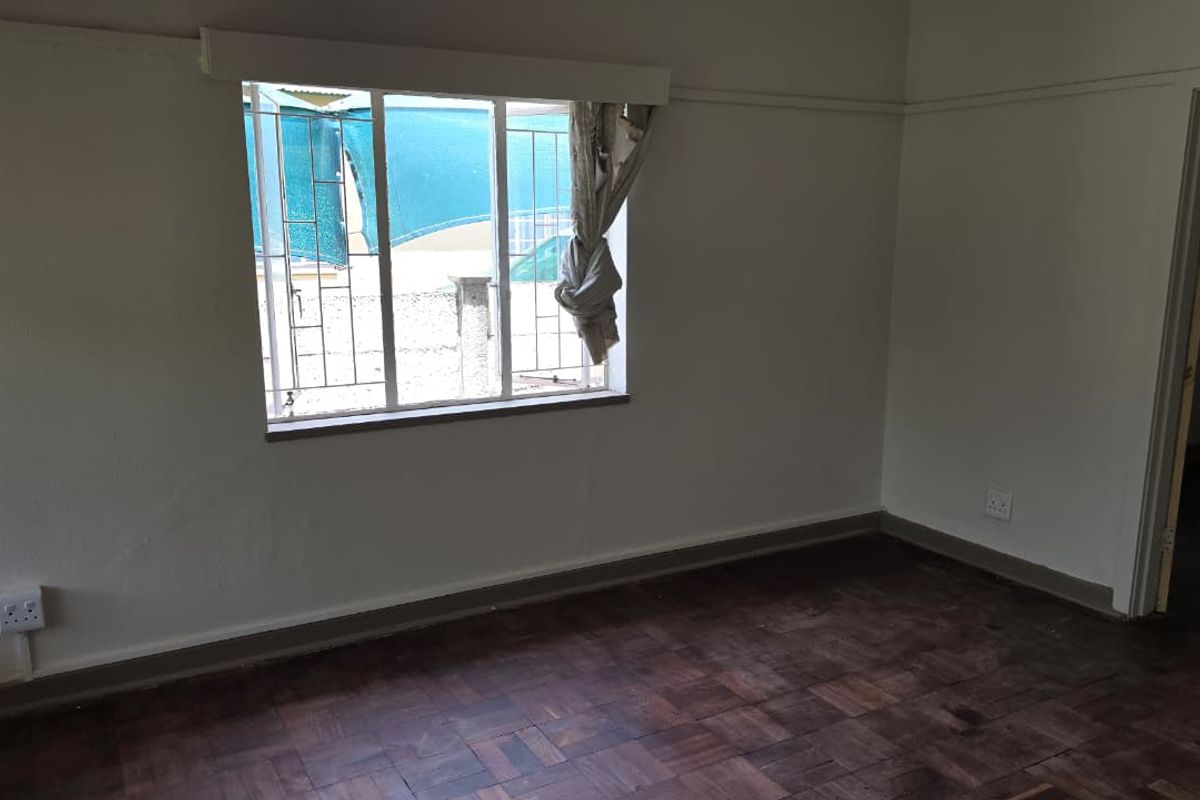 An empty bedroom featuring original parquet flooring, security bars on the window, and neutral wall finishes, ready for renovation or staging.