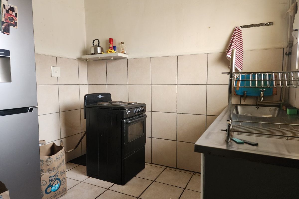 A functional kitchen area featuring tiled splashbacks, a stainless steel sink, and a freestanding stove, requiring some cosmetic updates to improve its overall condition.