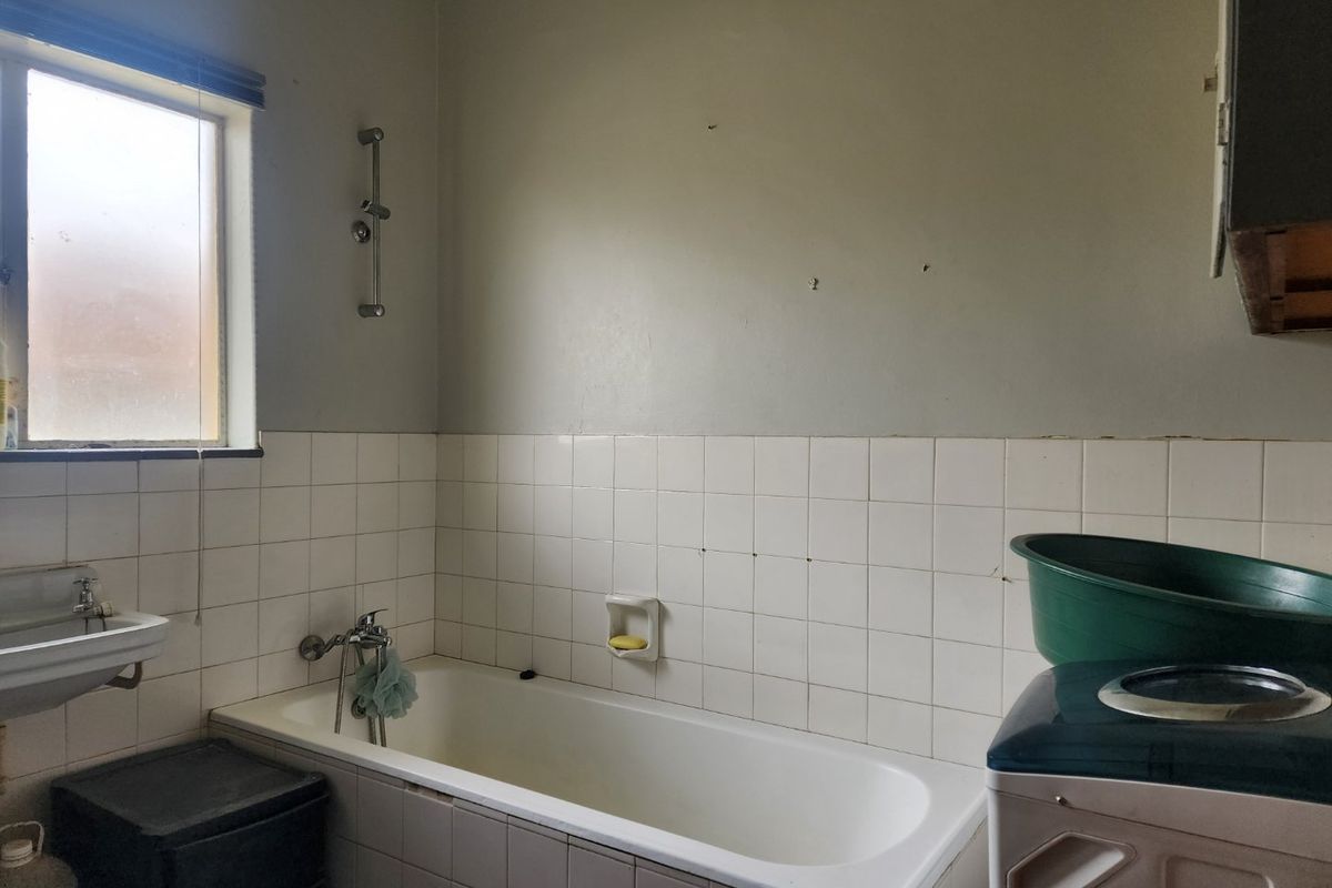 A dated bathroom featuring a standard bathtub, wall-mounted basin, and tiled splashback, requiring cosmetic updates and repairs to wall finishes.