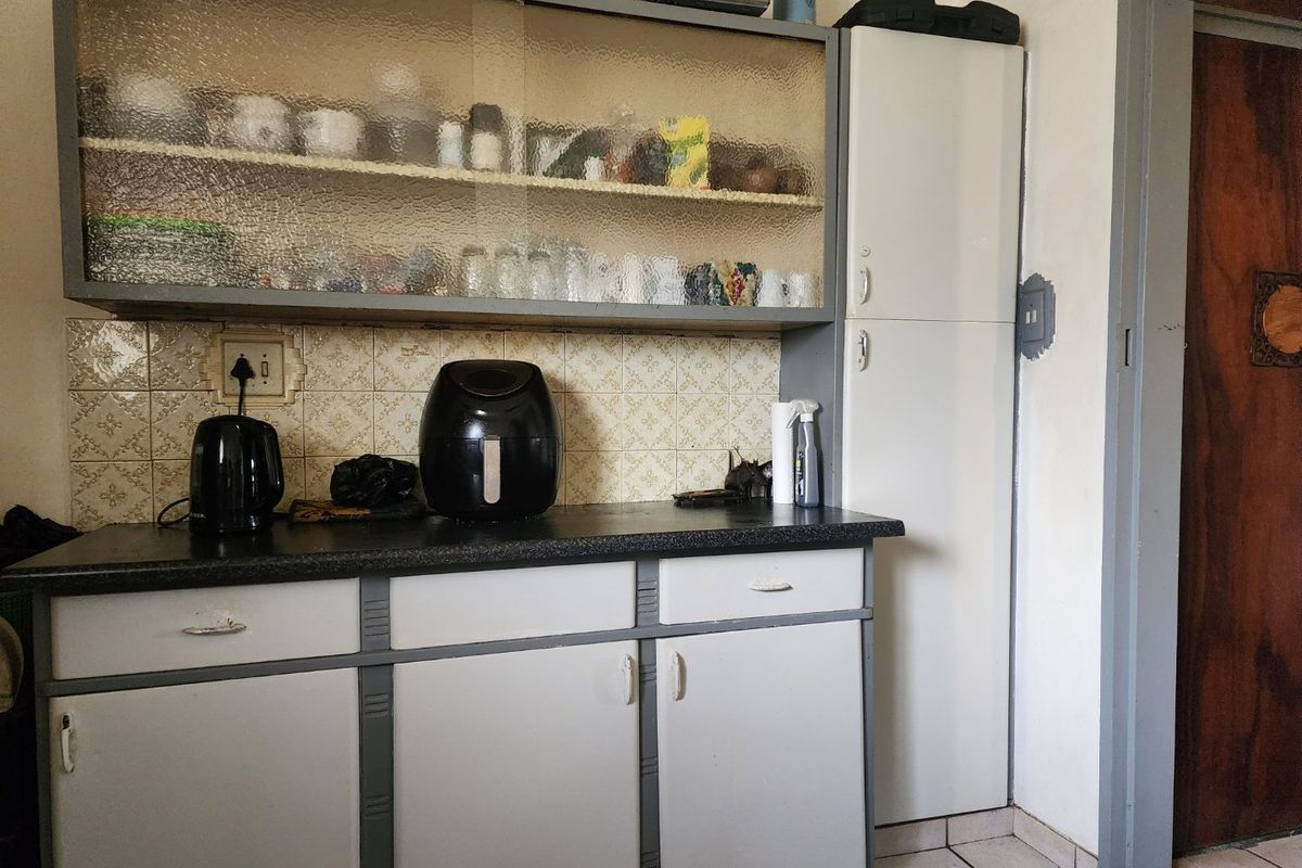 A dated kitchen area featuring built-in cabinetry with textured glass upper units, laminate countertops, and a tiled backsplash.