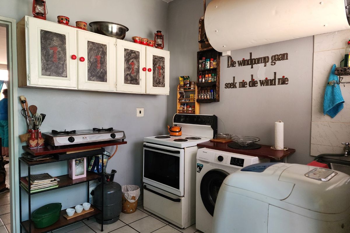 A compact kitchen featuring wall-mounted cabinetry, a freestanding electric stove, a gas cooktop, and tiled flooring, requiring modernization of finishes and utility management.