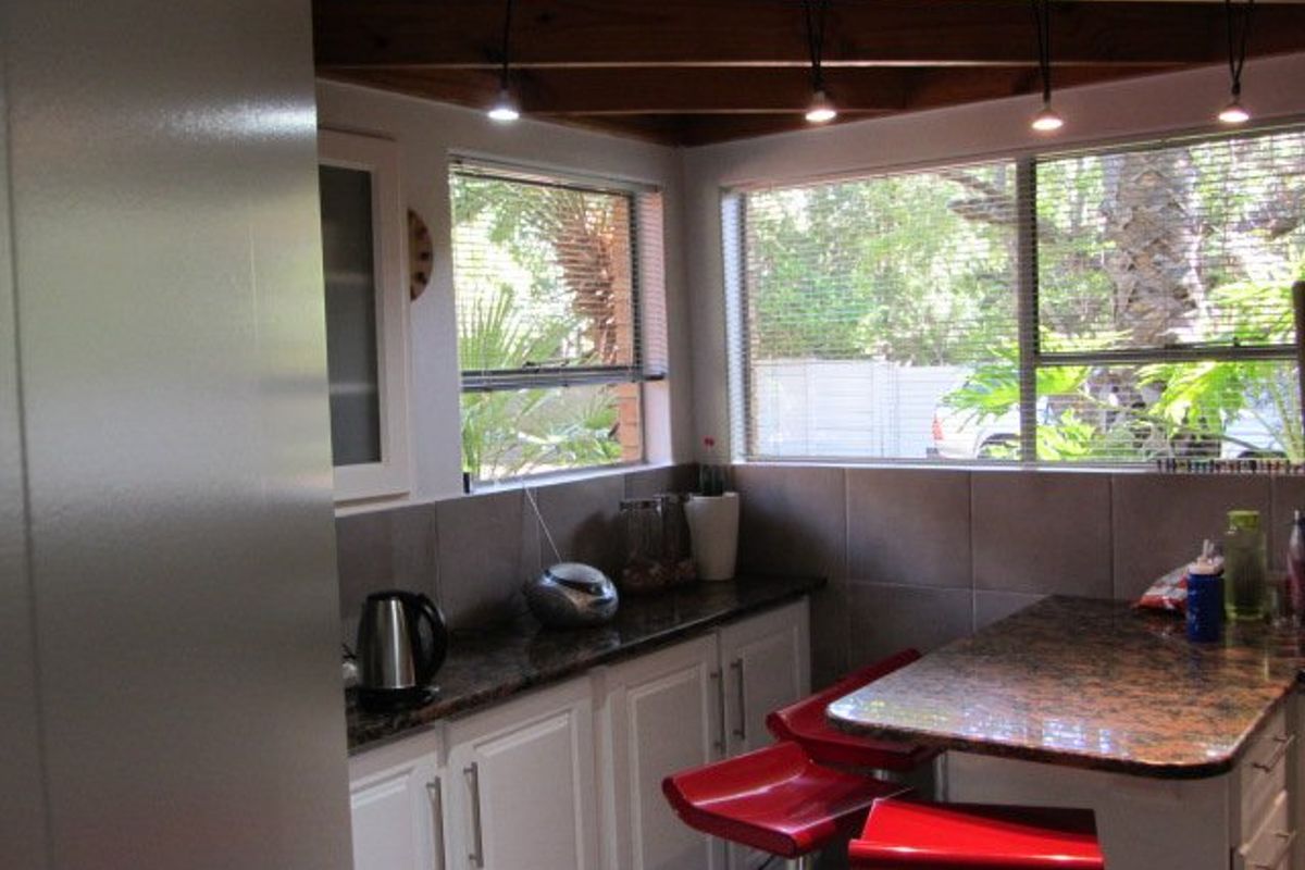 A kitchen area featuring granite countertops, tiled backsplash, and exposed timber ceiling beams with pendant lighting, offering a functional workspace with garden views.