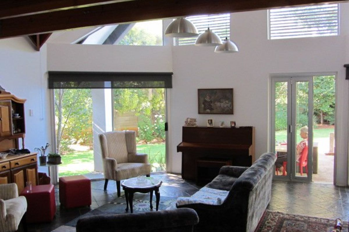 Spacious living area featuring high ceilings with exposed timber beams, slate flooring, and large glass doors providing seamless access to the garden.