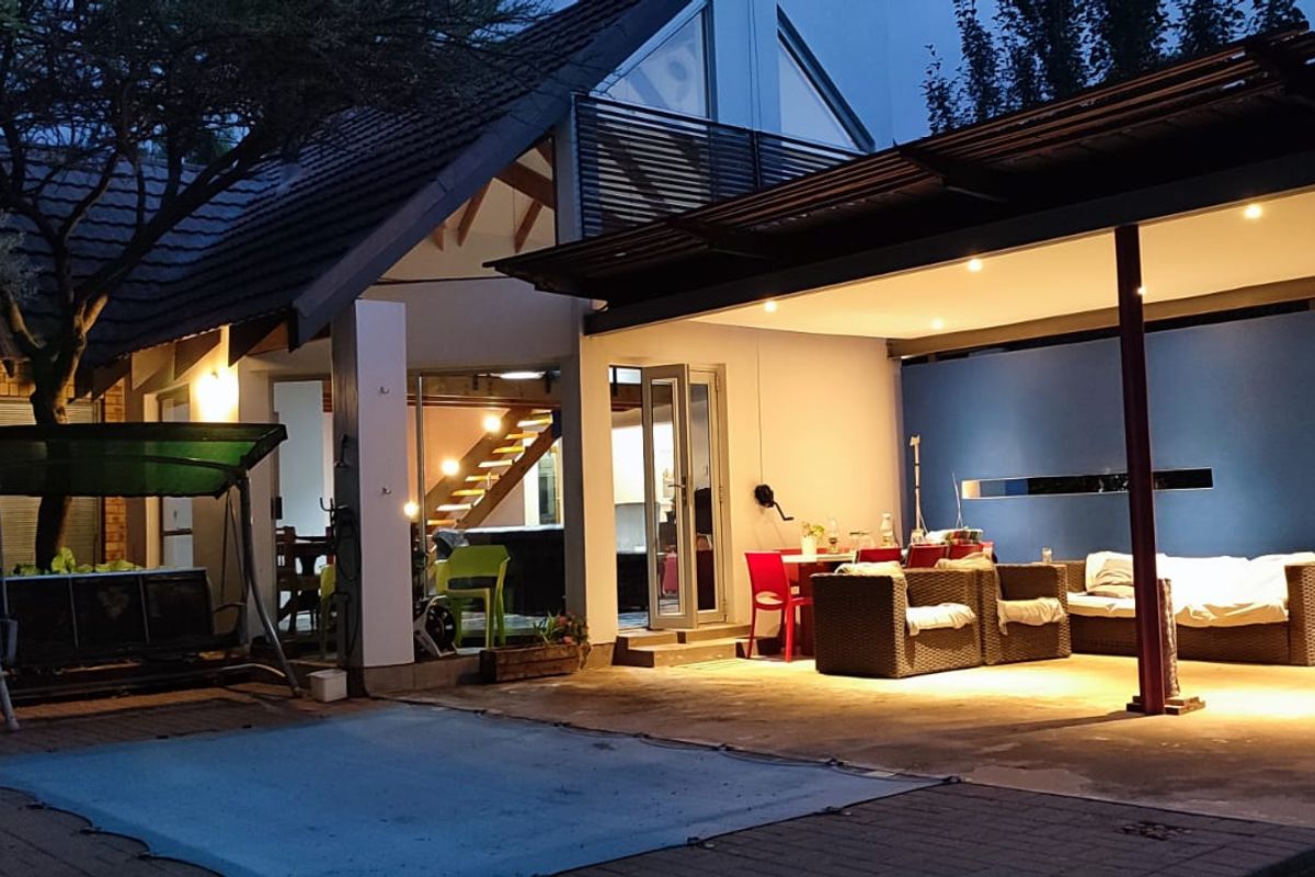 A rear exterior view of the house featuring a spacious covered patio with recessed lighting, overlooking a paved area and garden.