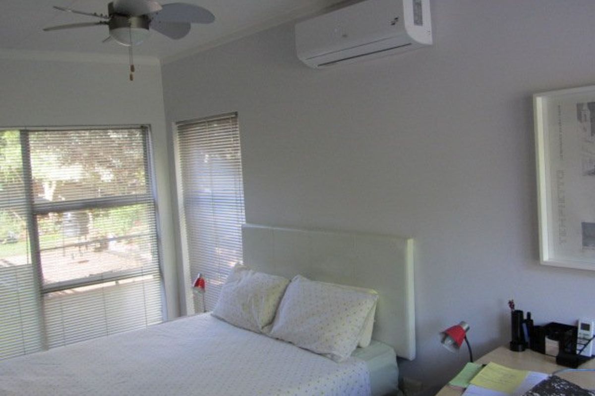 A well-maintained bedroom featuring a ceiling fan, split-system air conditioning, and large windows with venetian blinds.