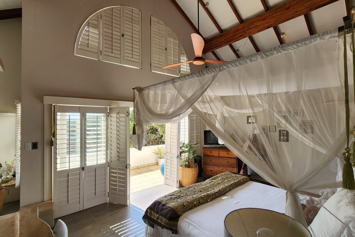 Spacious bedroom featuring vaulted ceilings with exposed timber beams, arched shutters, and direct access to a private balcony through double doors.