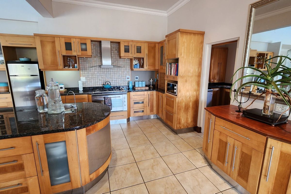 Spacious kitchen featuring light wood cabinetry, granite countertops, a central island, and a tiled backsplash with integrated stainless steel appliances.