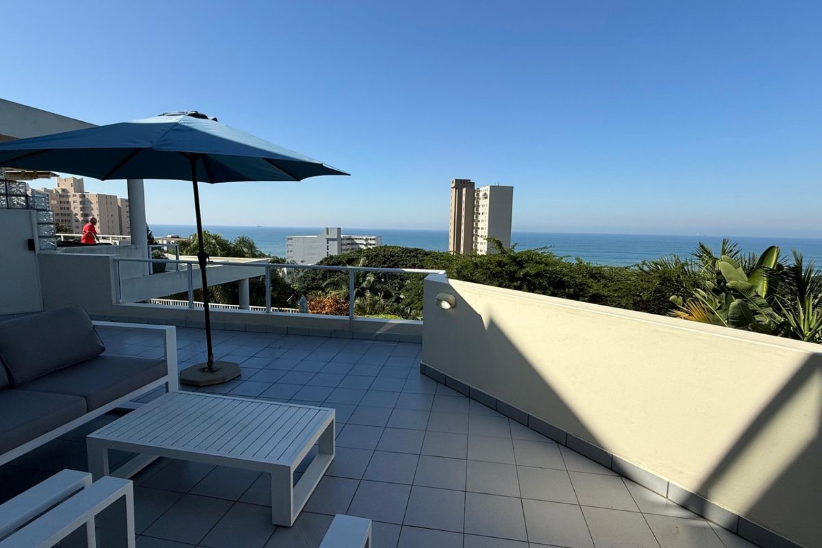 Spacious balcony featuring tiled flooring, a glass balustrade, and a masonry parapet wall, offering expansive ocean and coastal views.