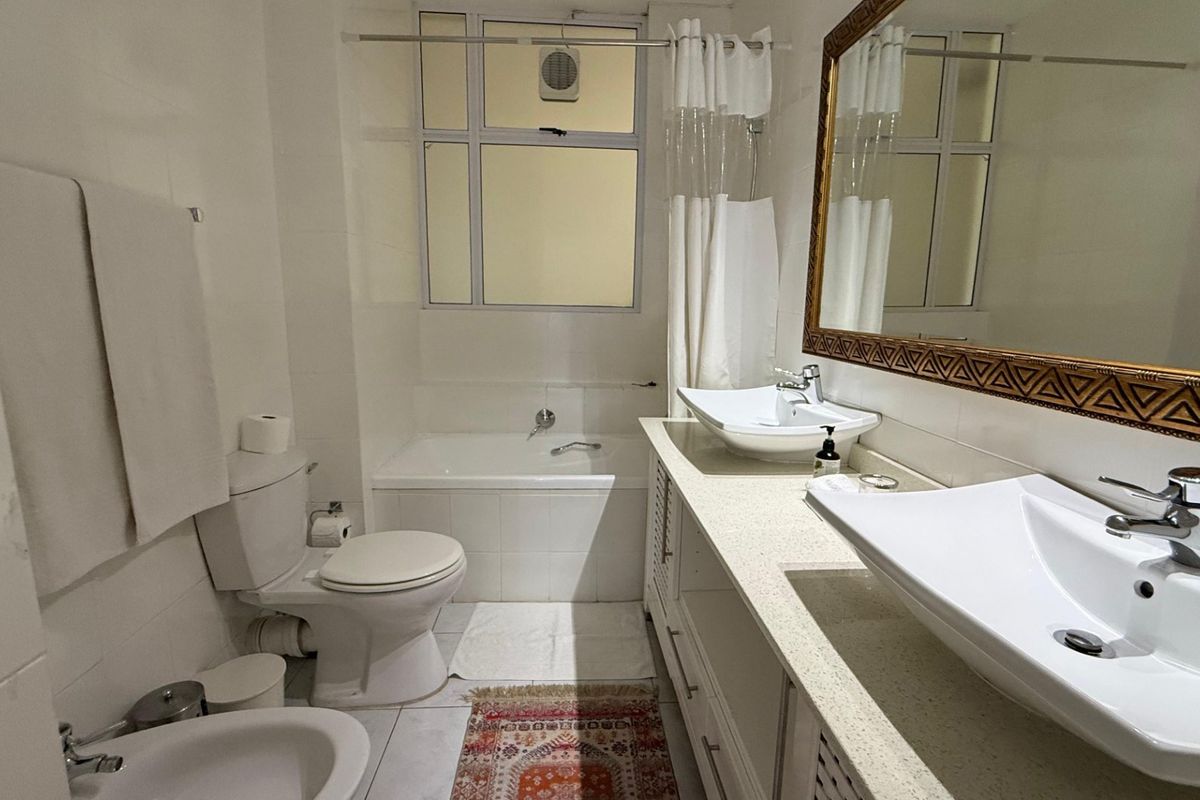 A well-maintained bathroom featuring a dual vanity with vessel sinks, a bathtub, a bidet, and a toilet, finished with clean white tiling.