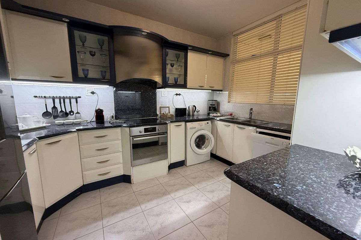 A functional kitchen featuring granite countertops, built-in oven, electric hob, extractor fan, and integrated laundry appliance space with ample cabinetry.