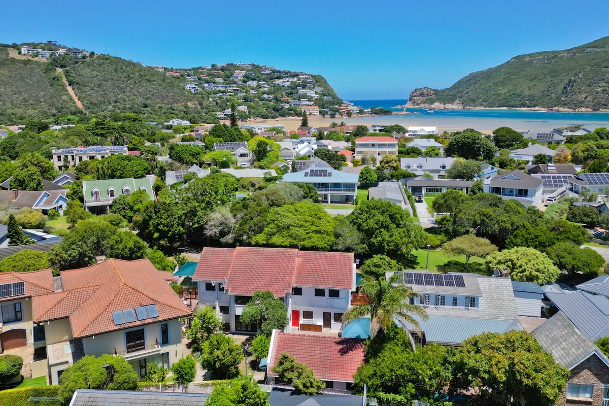Aerial view of a residential neighborhood featuring homes with tiled roofs and solar panels, situated near a coastal lagoon and hills.