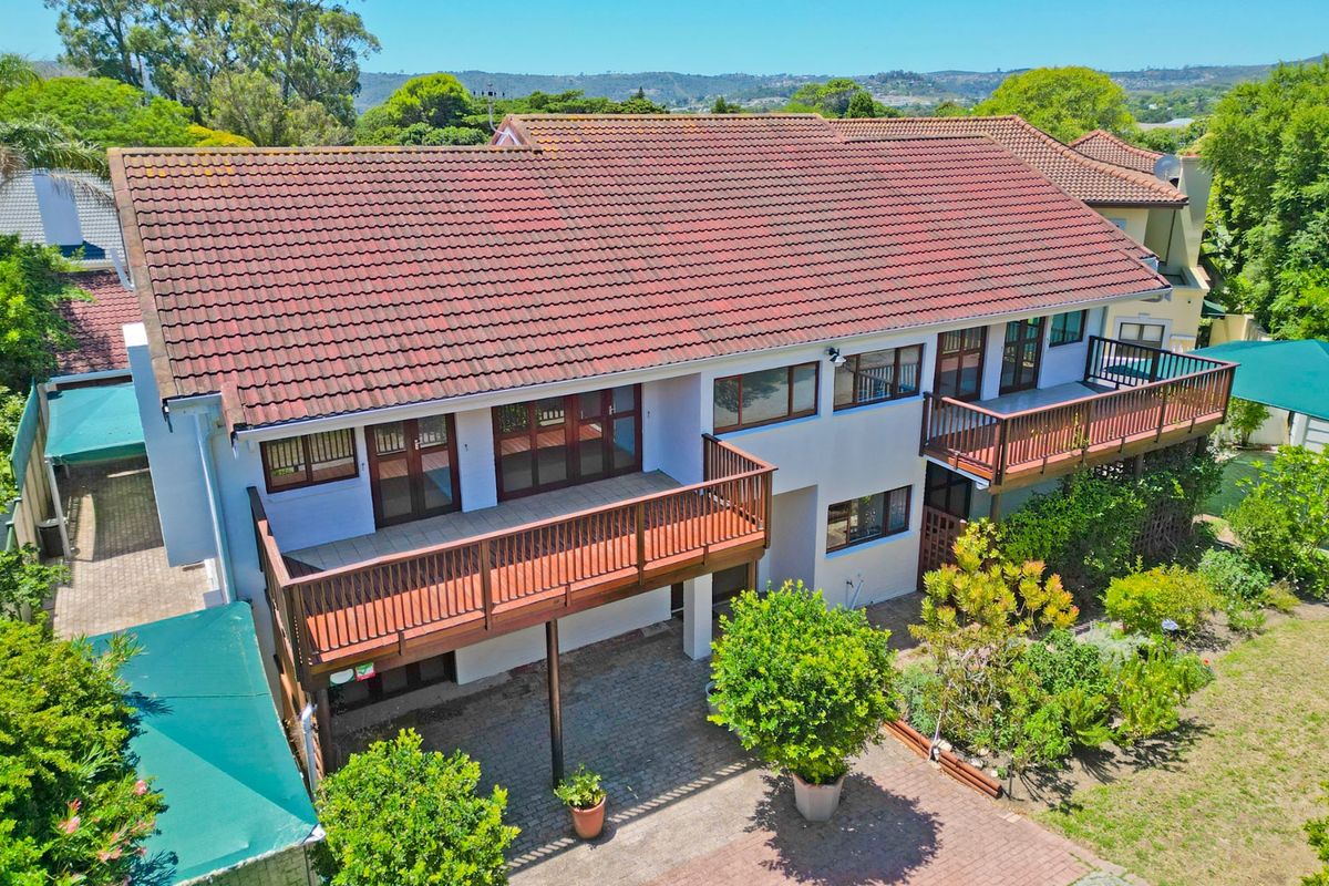 Aerial view of the rear elevation featuring a double-storey design with wooden balconies, paved patio area, and a tiled roof.
