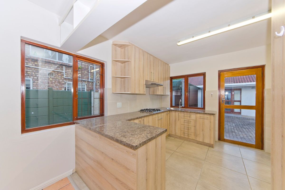A clean, functional kitchen featuring light wood-look cabinetry, granite countertops, a gas hob, and direct access to the exterior.