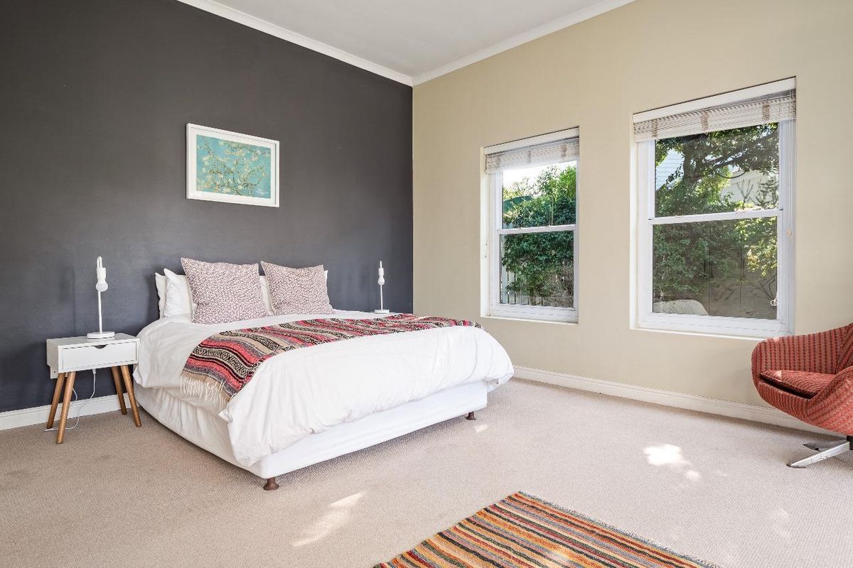 A well-lit bedroom featuring neutral carpeting, a dark accent wall, and dual sash windows providing natural light and garden views.