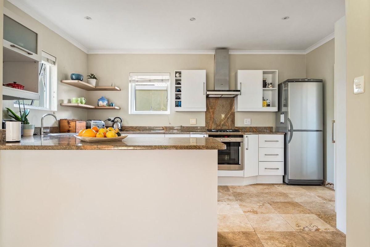 A functional kitchen featuring granite countertops, built-in cabinetry, a gas hob with extractor fan, and durable stone tile flooring.
