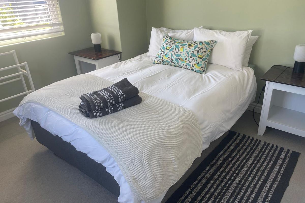 A functional bedroom featuring neutral wall tones, carpeted flooring, and venetian blinds, providing a comfortable and well-lit sleeping space.