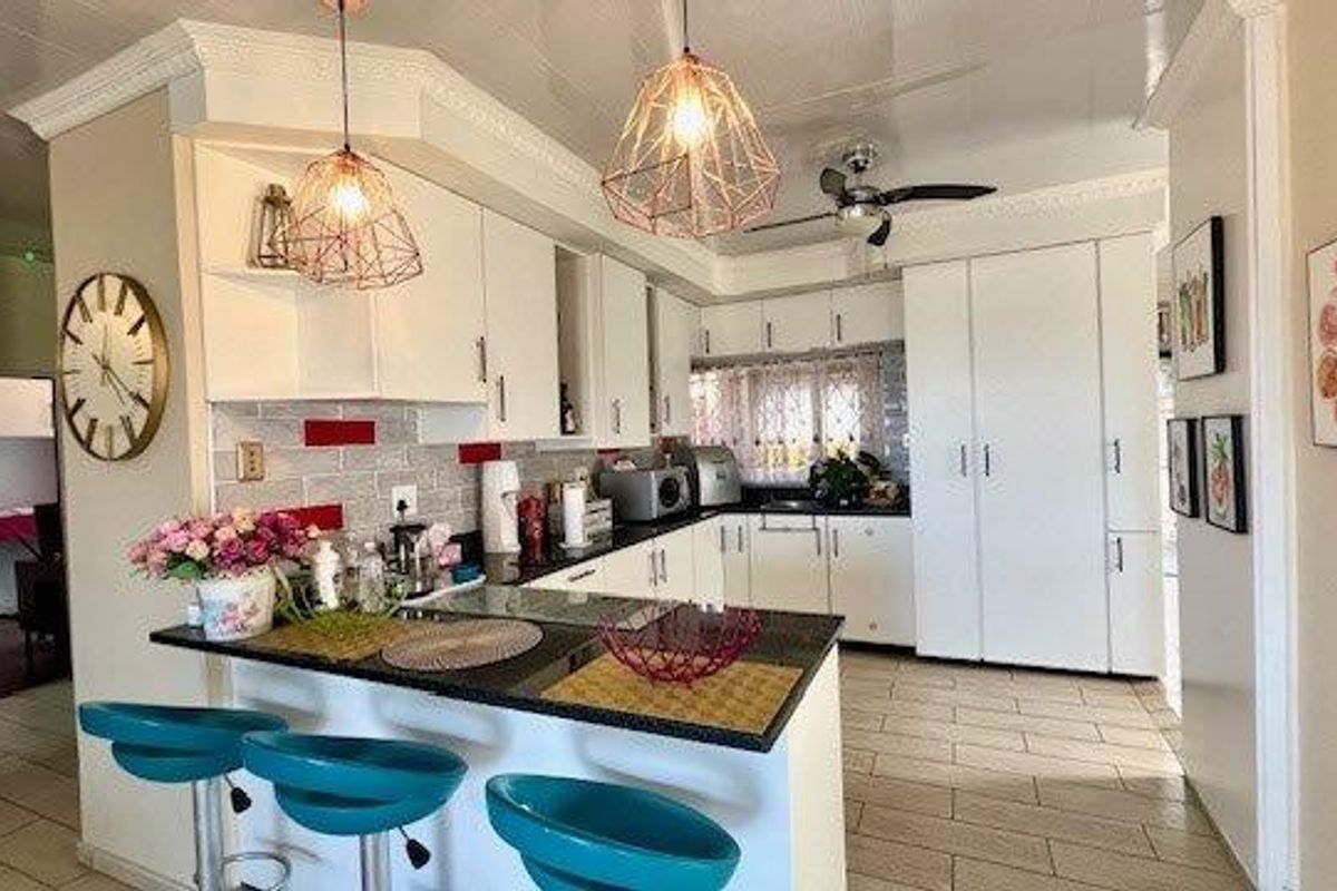 A functional kitchen featuring white cabinetry, granite countertops, a breakfast bar, and modern pendant lighting, complemented by tiled flooring and a tiled backsplash.
