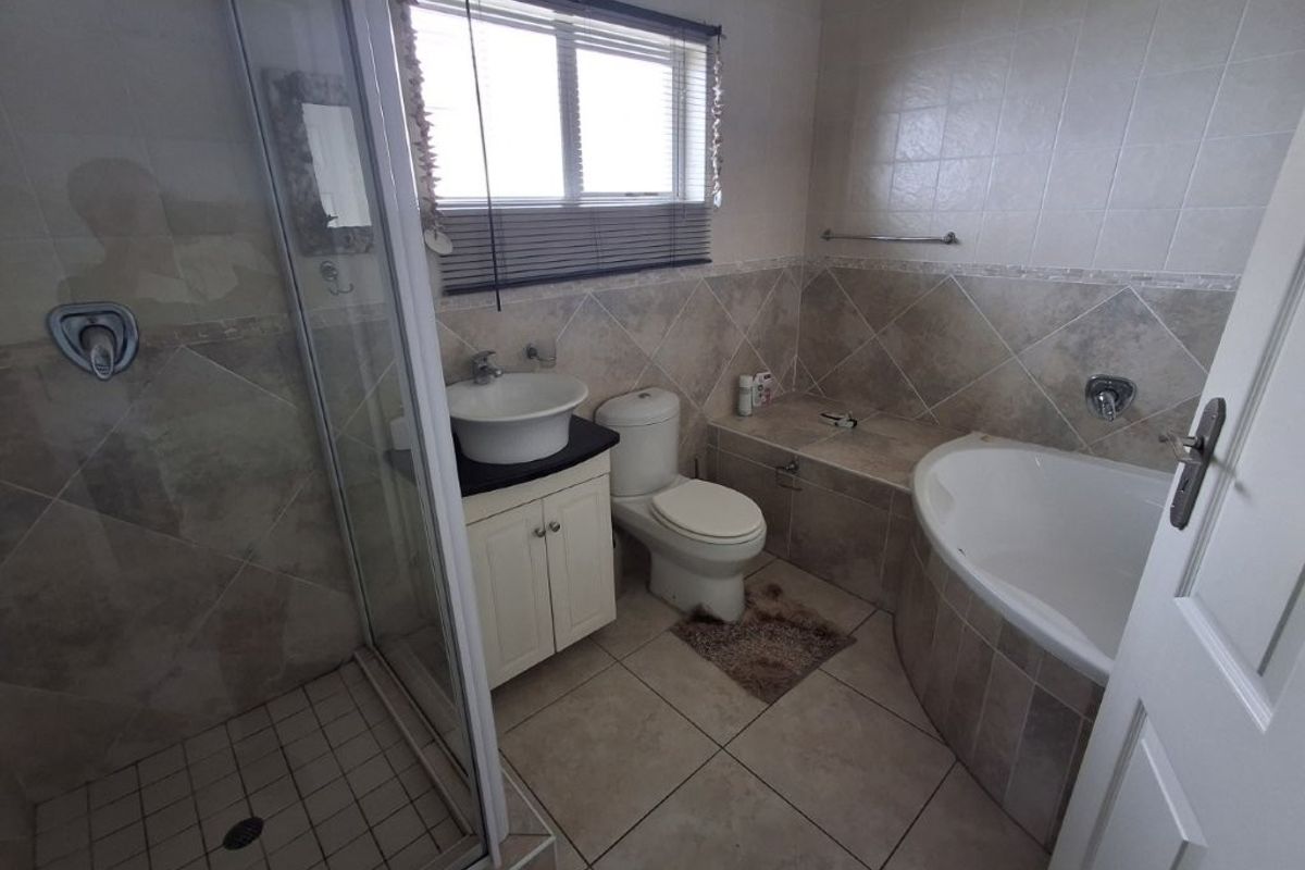 A functional bathroom featuring a corner bathtub, separate shower enclosure, vanity with vessel sink, and neutral wall and floor tiling.