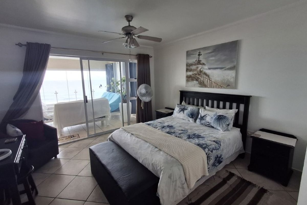 Spacious bedroom featuring tiled flooring, a ceiling fan, and large sliding glass doors providing direct access to a private balcony with ocean views.