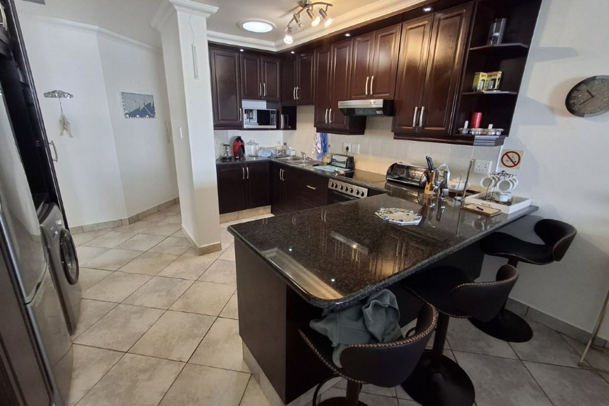 A functional kitchen featuring dark wood cabinetry, granite countertops, a breakfast bar, and integrated appliances, finished with tiled flooring.