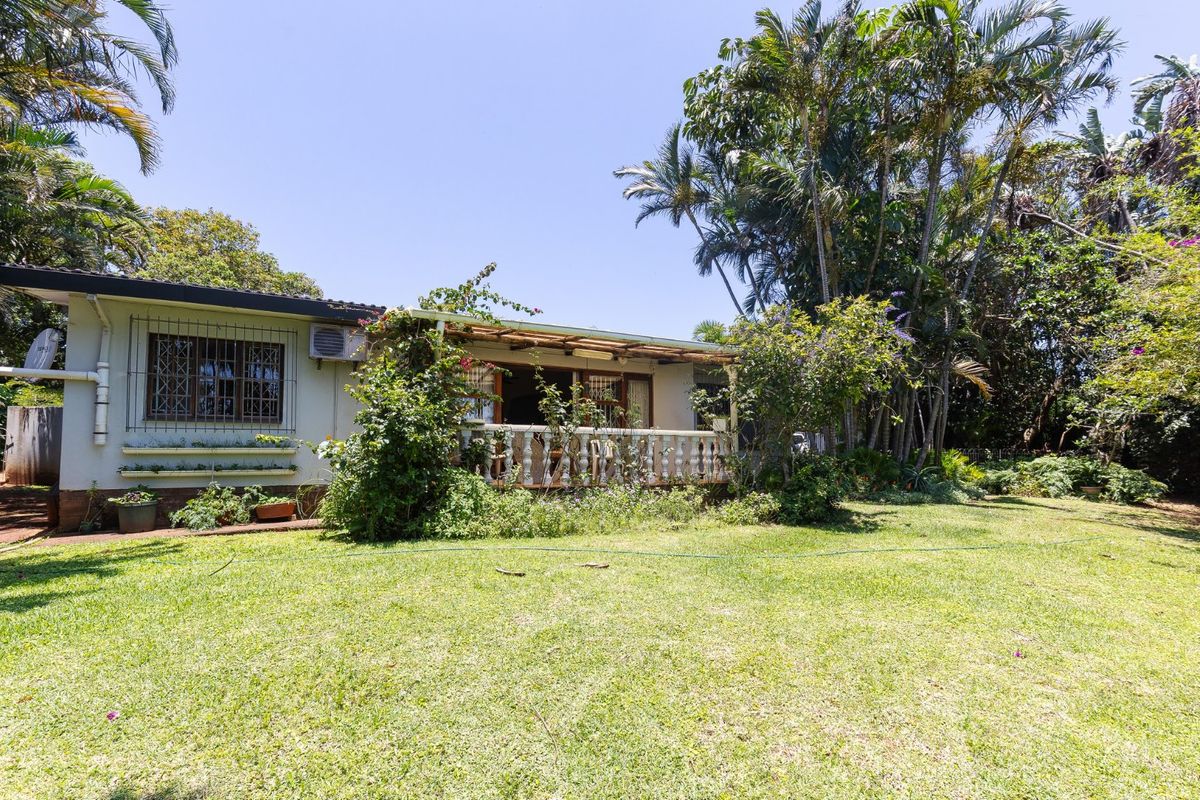 Rear view of the house featuring a covered patio with a balustrade, set within a spacious garden with mature trees.