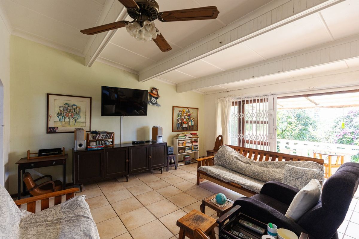 A living room featuring exposed ceiling beams, a ceiling fan, and ceramic tiled flooring, with direct access to an outdoor patio area.