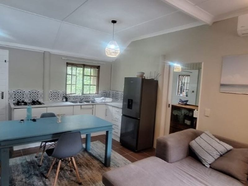 Open-plan living and kitchen area featuring tiled flooring, built-in cabinetry with a gas hob, and a wall-mounted air conditioning unit.