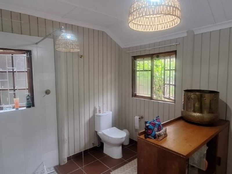 A functional bathroom featuring a shower, toilet, tiled flooring, and timber wall paneling with security bars on the windows.