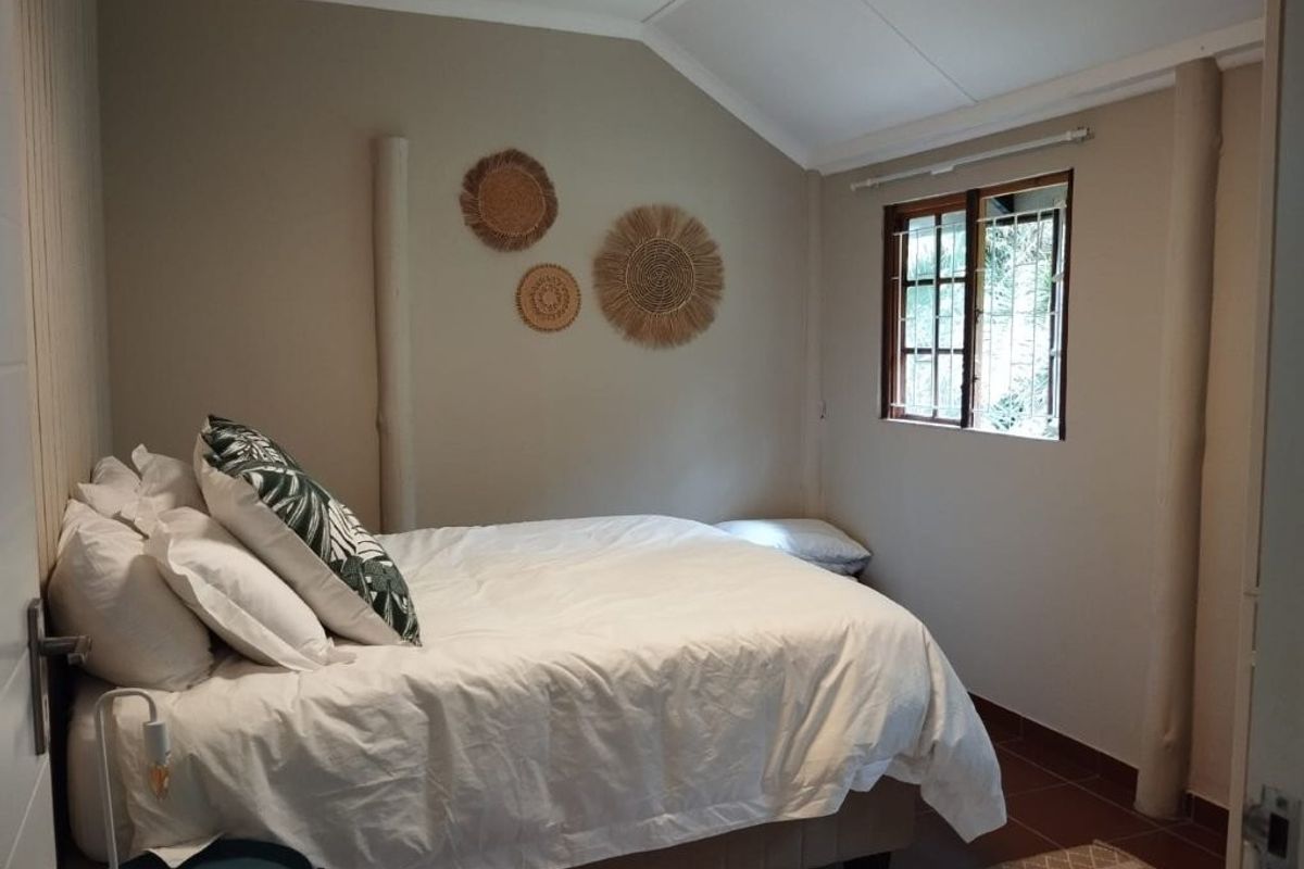 A cozy bedroom featuring a vaulted ceiling, tiled flooring, and a timber-framed window with security bars.