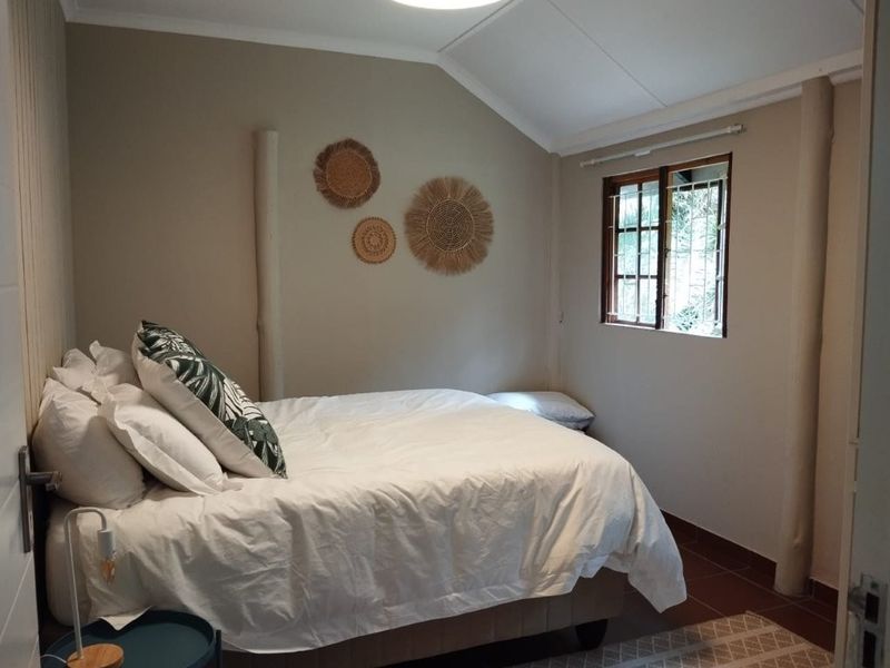 A cozy bedroom featuring a vaulted ceiling, tiled flooring, and a timber-framed window with security bars.