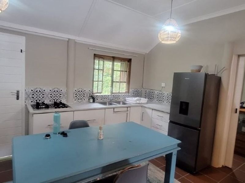 A functional kitchen featuring built-in cabinetry, a gas hob, tiled backsplash, and tiled flooring, with an adjacent doorway leading to a secondary space.