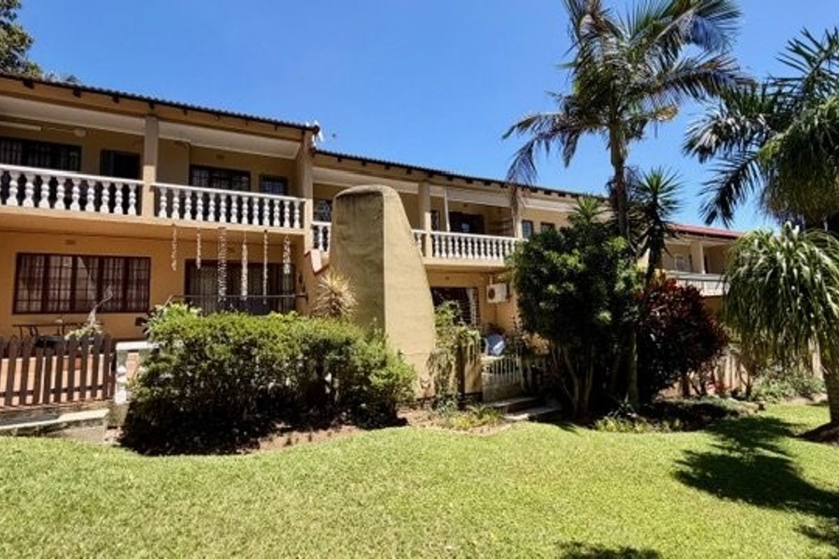 Rear view of a multi-level townhouse featuring a lawn, paved patio area, and upper-level balconies with balustrades.