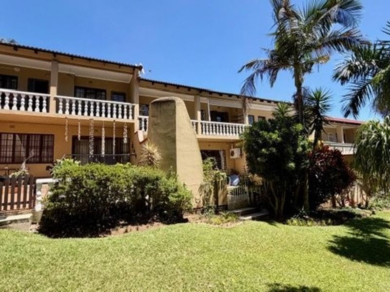 Rear view of a multi-level townhouse featuring a lawn, paved patio area, and upper-level balconies with balustrades.