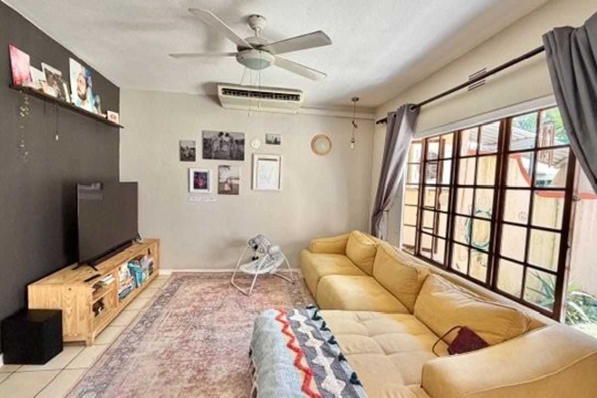 A comfortable living room featuring tiled flooring, a ceiling fan, and a wall-mounted air conditioning unit, with large windows providing natural light.