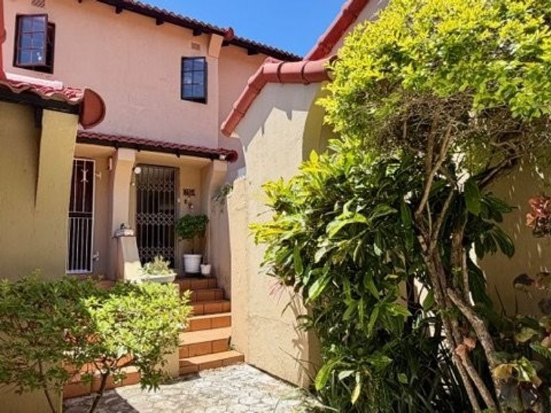 Front entrance of the townhouse featuring a tiled staircase, security gate, and terracotta roof tiles with established garden landscaping.