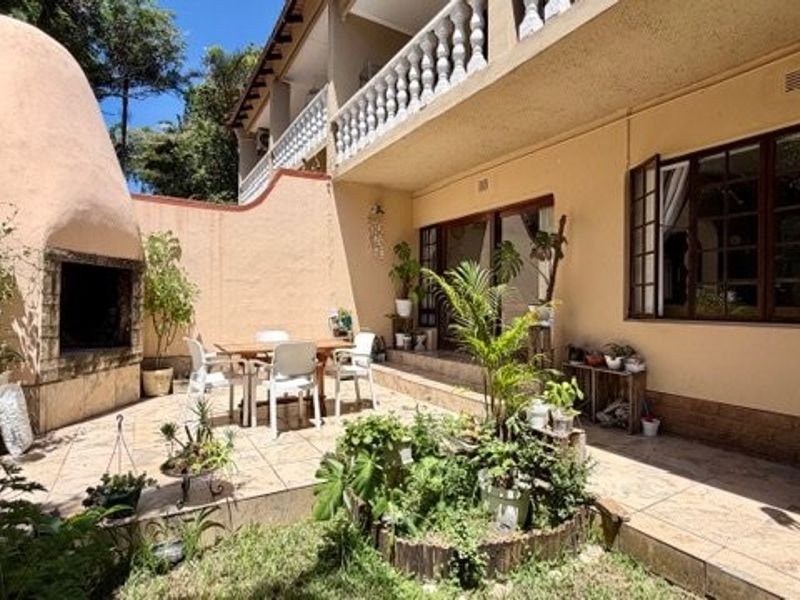 A spacious outdoor patio featuring a built-in braai, tiled flooring, and direct access to the home through sliding doors, perfect for outdoor entertaining.