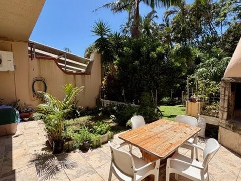 Covered patio area featuring stone tile flooring and a built-in braai, overlooking a private garden space.