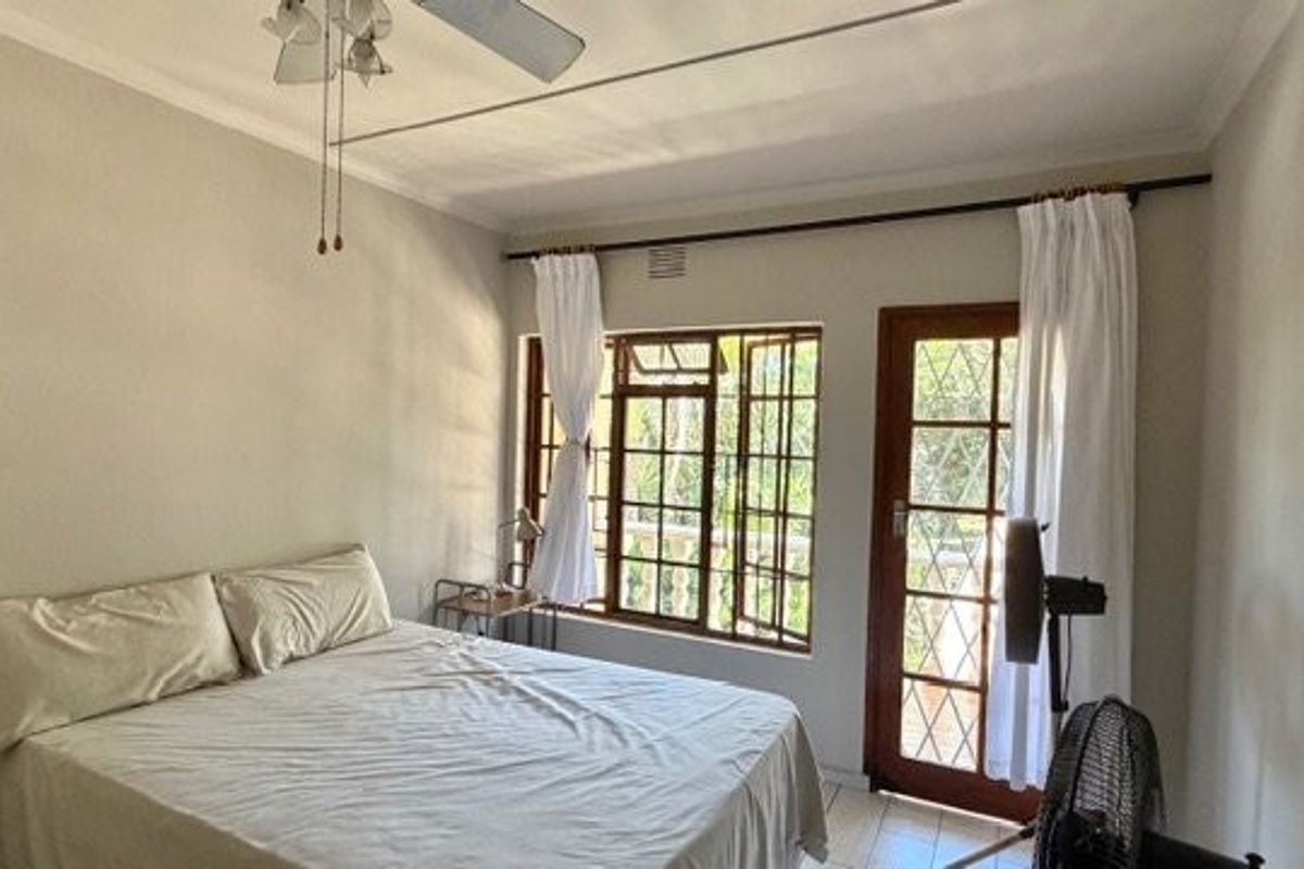 A bedroom featuring a ceiling fan, casement windows, and a timber-framed glass door providing access to the exterior.
