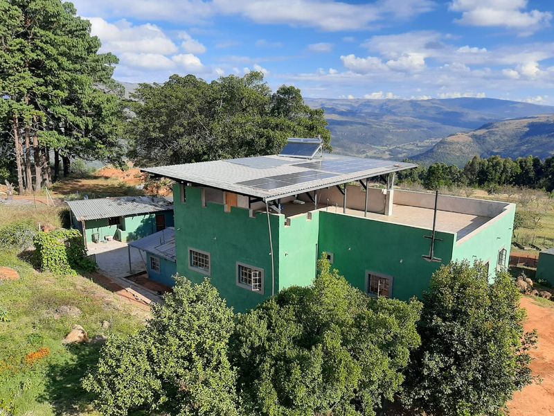 Aerial view of a green farm house featuring a metal roof with integrated solar panels, a solar water heater, and a flat roof terrace.