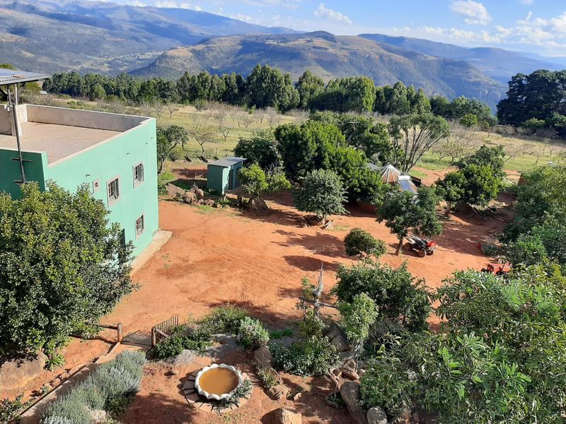 An elevated aerial view of the farm property, showcasing the main farmhouse, surrounding garden, and expansive mountain landscape views.