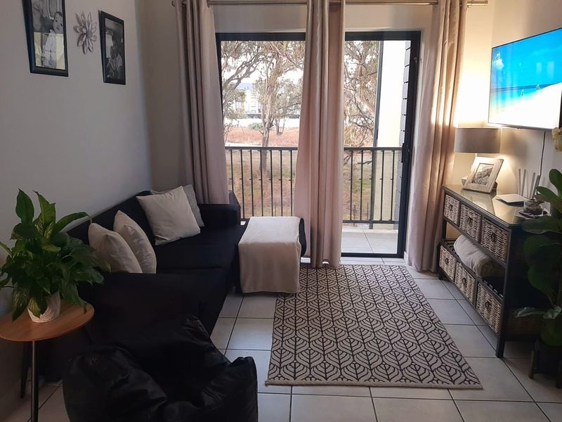 A cozy living room featuring tiled flooring and a sliding glass door that opens onto a balcony with outdoor views.
