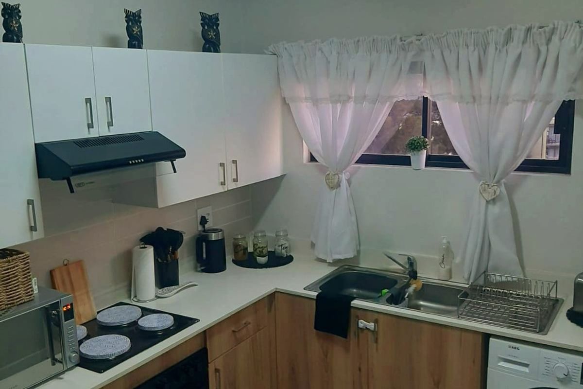 A functional kitchen featuring wood-look lower cabinetry, white upper cabinets, tiled flooring, and integrated appliances including an oven, hob, and washing machine connection.