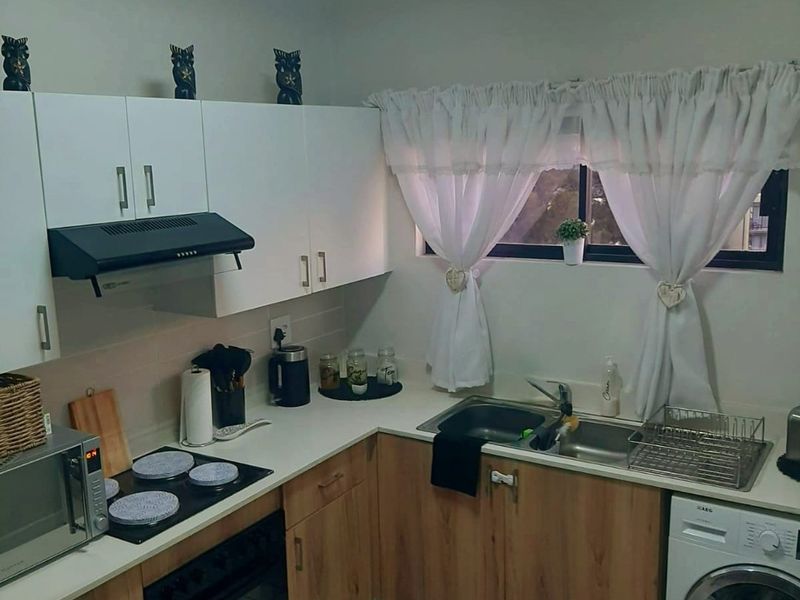 A functional kitchen featuring wood-look lower cabinetry, white upper cabinets, tiled flooring, and integrated appliances including an oven, hob, and washing machine connection.