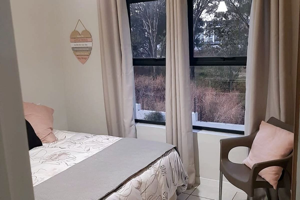 A well-maintained bedroom featuring neutral tiled flooring, large aluminium-framed windows, and a simple pendant light fixture, offering a clean and functional living space.