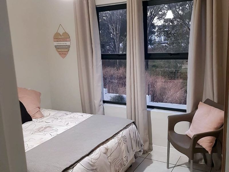 A well-maintained bedroom featuring neutral tiled flooring, large aluminium-framed windows, and a simple pendant light fixture, offering a clean and functional living space.