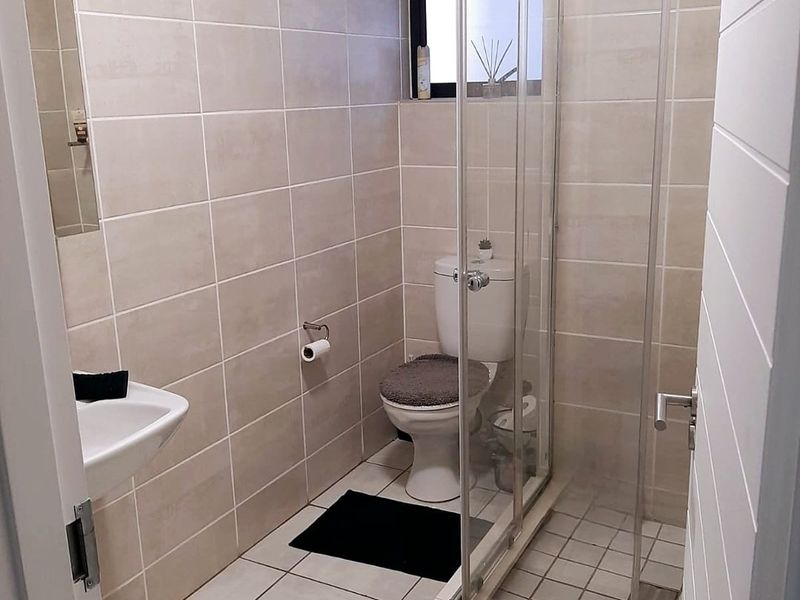 A functional bathroom featuring a glass shower enclosure, wall-mounted basin, and neutral floor-to-ceiling wall tiling.