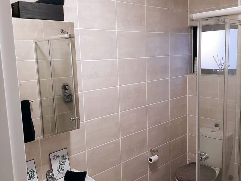A compact, well-maintained bathroom featuring neutral wall tiling, a pedestal basin, a shower enclosure, and a toilet.