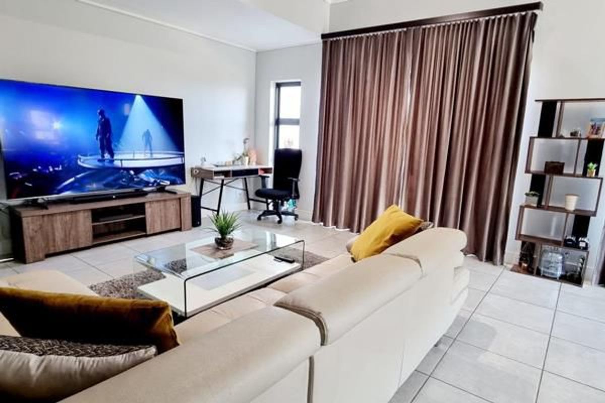 A well-maintained living room featuring neutral tiled flooring, large windows with full-length curtains, and a spacious layout suitable for relaxation.