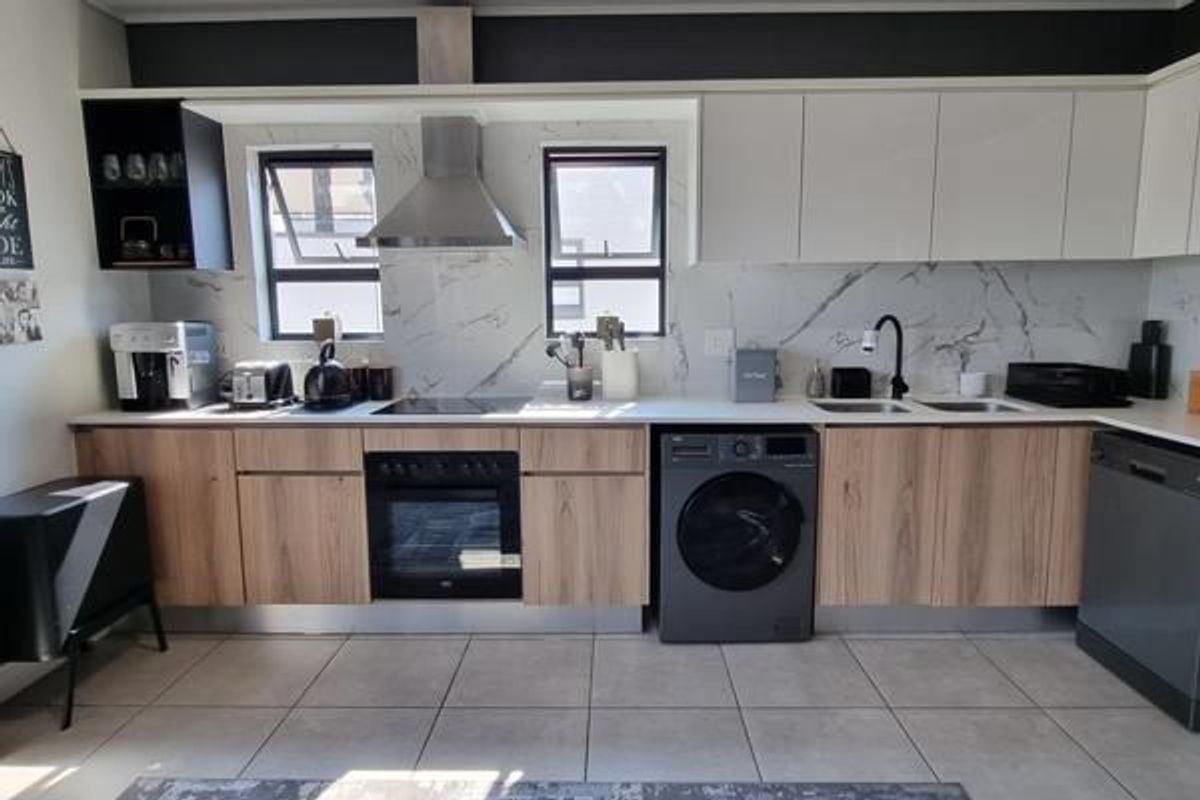 Modern kitchen featuring light wood-grain cabinetry, marble-look splashback, stainless steel extractor fan, built-in oven, and integrated sink with contemporary fixtures.